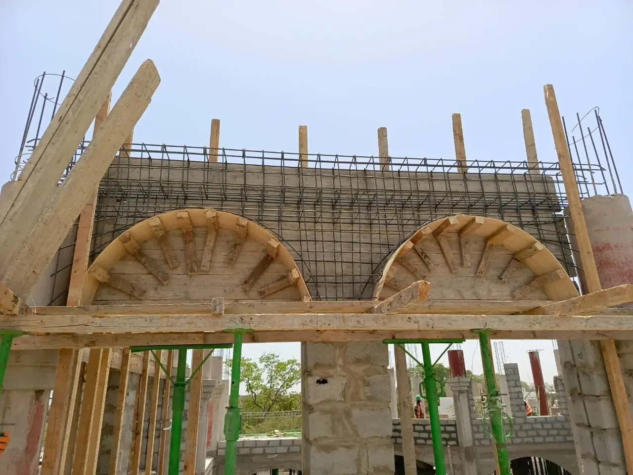 Timber formwork of two arches topped with rebar, green props
