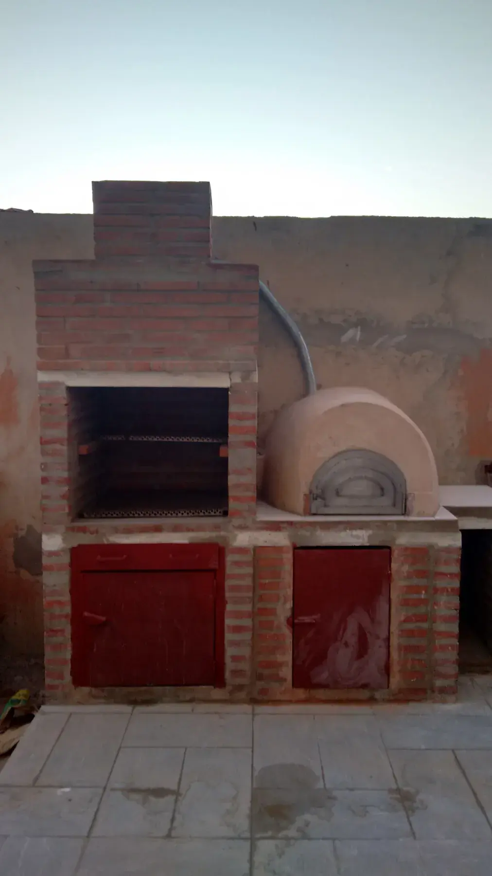 Barbecue en briques avec four à dôme intégré et portes métalliques rouges