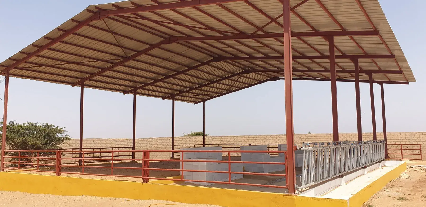 Structure acier rouge d'un bâtiment d'élevage avec toiture en tôle et auge carrelée