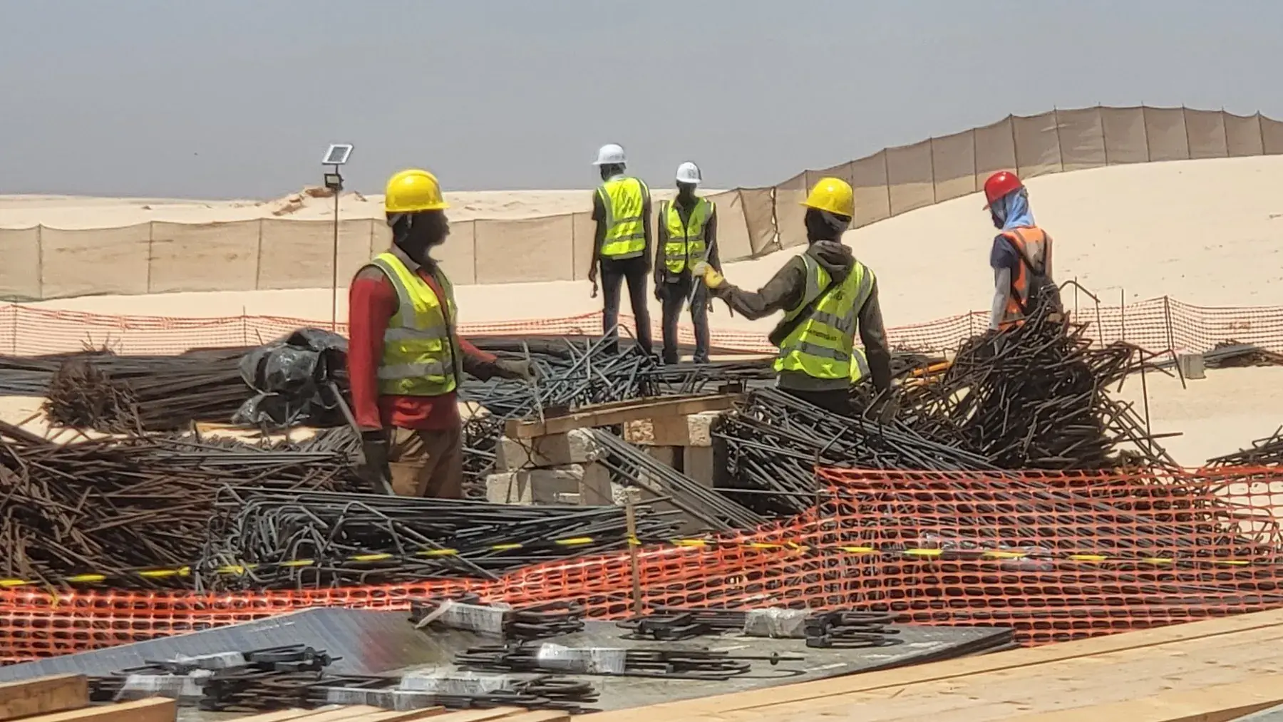 Équipe chantier en casques et gilets haute visibilité au travail sur un tas d'armatures