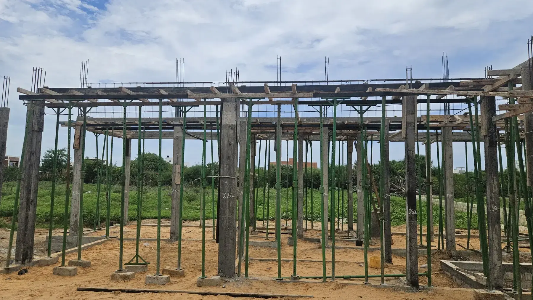 Ossature en béton armé avec poteaux et étaiements verts sous un ciel nuageux
